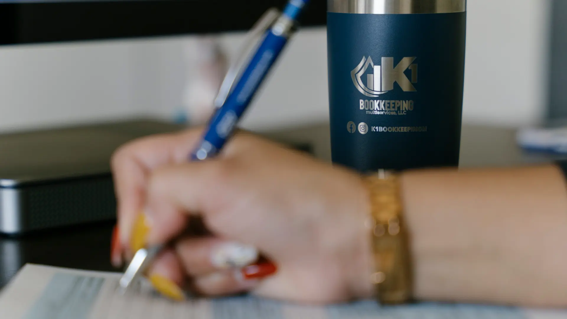 A K1 Bookkeeping team member writing on a client file next to a branded K1 tumbler